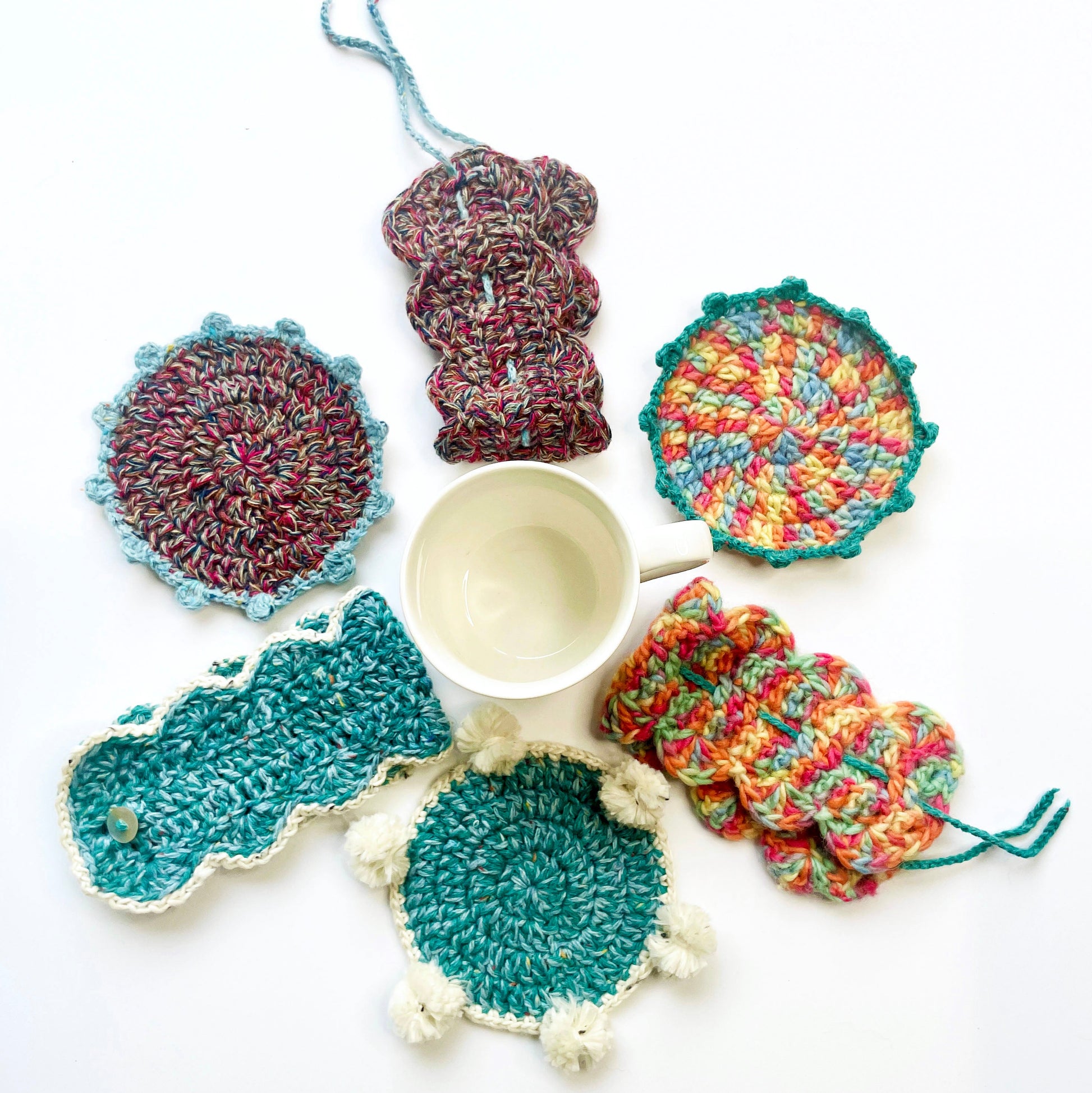 Colourful crochet coasters and mug wraps on a white background